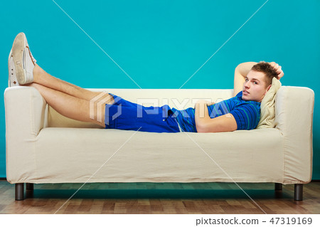 Young man relaxing on couch on blue Young man relaxing on couch on blue 47319169