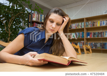 Girl reading a book at the table in the library 47320484