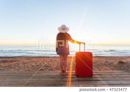 Holiday, travel and tourism concept - Beautiful women with red suitcase over sandy beach background 47323477