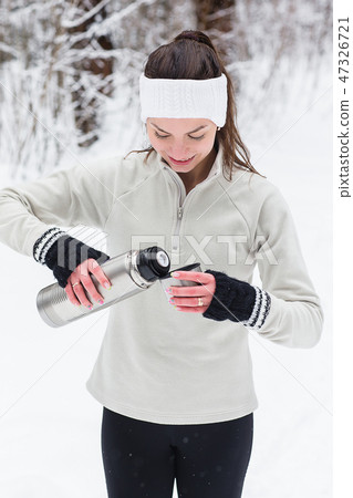 Woman pours and drinks tea from a thermos after jogging Woman pours and drinks tea from a thermos after jogging 47326721