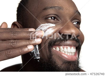 Young african-american guy applying face cream under his eyes on white background 47326740