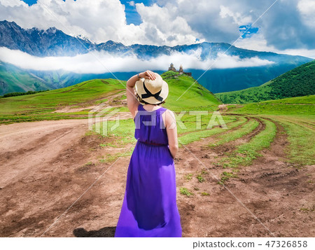 The scenic view from Kazbegi Georgia. Girl in long dress and hat stands and looks at the church of The scenic view from Kazbegi Georgia. Girl in long dress and hat stands and looks at the church of 47326858
