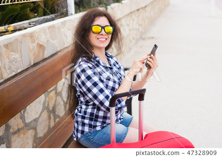 Technology, travelling and people concept - young woman sit on bench in sunny glasses and typing on Technology, travelling and people concept - young woman sit on bench in sunny glasses and typing on 47328909