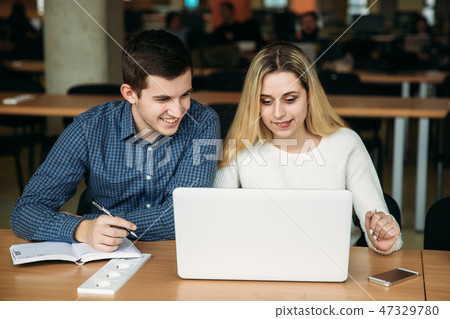 Boy and girl sits in universiti library. They use laptop to prepare for an exam. Study 47329780