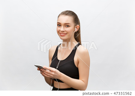 Isolated shot of young sportswoman has healthy athleteic body, listens music with headphones, holds Isolated shot of young sportswoman has healthy athleteic body, listens music with headphones, holds 47331562