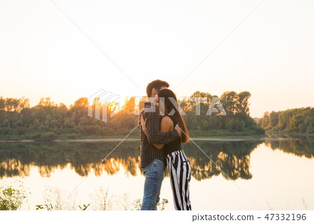 Romantic and people concept - young couple hugging together near the river or lake and enjoying Romantic and people concept - young couple hugging together near the river or lake and enjoying 47332196