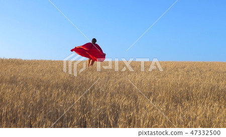 young girl in red raincoat plays in superhero runs across field of yellow wheat against a blue sky young girl in red raincoat plays in superhero runs across field of yellow wheat against a blue sky 47332500
