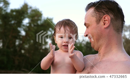 Small wet bathing child claps his hands and laughs sitting in embrace of dad Small wet bathing child claps his hands and laughs sitting in embrace of dad 47332665