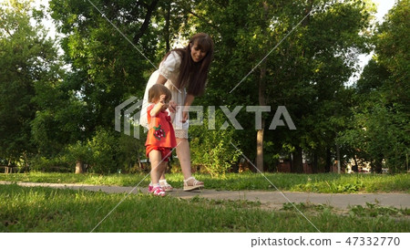 Mom and little daughter are walking along path in the summer park. baby's first steps with mom 47332770
