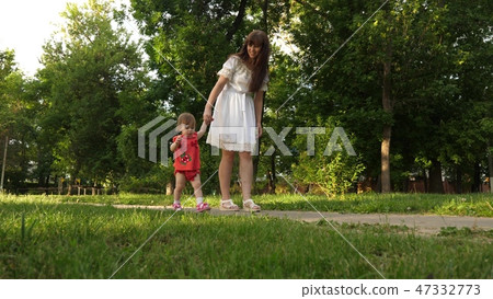 Mom and little daughter are walking along path in the summer park. baby's first steps with mom 47332773