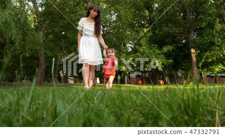 child and mother walk on green lawn grass in the summer city Park and smiling. child and mother walk on green lawn grass in the summer city Park and smiling. 47332791