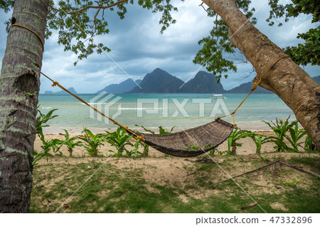 Traditional braided hammock in the shade with tropical island in the background Traditional braided hammock in the shade with tropical island in the background 47332896