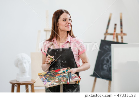 A young woman painter in a bright white studio draws a picture on canvas on an easel. A young woman painter in a bright white studio draws a picture on canvas on an easel. 47333158