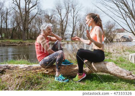 Senior and young woman resting on log after sport 47333326
