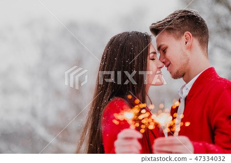 Young man and woman kiss in the winter in the park. Red clothes. In the hands of burning fireworks 47334032