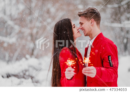 Young man and woman kiss in the winter in the park. Red clothes. In the hands of burning fireworks 47334033