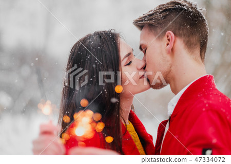Young man and woman kiss in the winter in the park. Red clothes. In the hands of burning fireworks 47334072