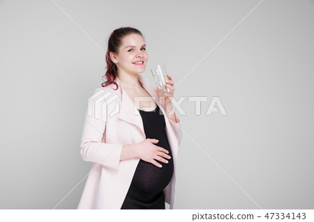 A pregnant girl is holding a glass of water and drinking. 47334143