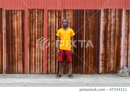 Young black African man standing against old rusty sheet wall Young black African man standing against old rusty sheet wall 47334311