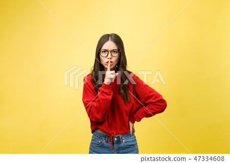 Young woman over yellow wall showing a sign of silence gesture putting finger in mouth Young woman over yellow wall showing a sign of silence gesture putting finger in mouth 47334608