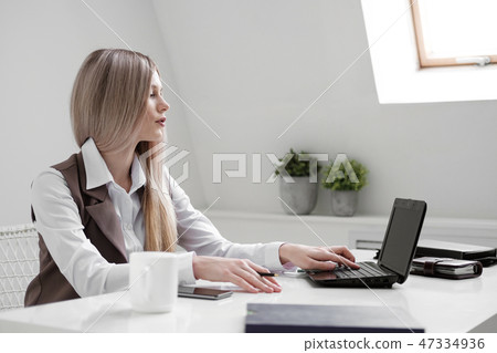 Blonde girl in a business suit works on a computer in a white bright office. Blonde girl in a business suit works on a computer in a white bright office. 47334936