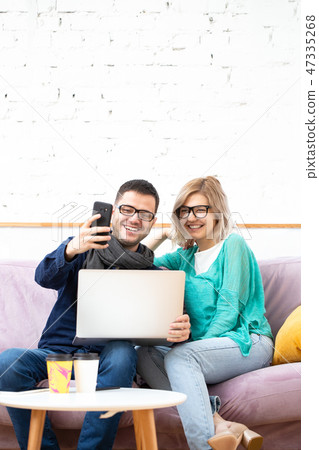Friends sit on the couch, chatting and using a smartphone, desktop computer. 47335268