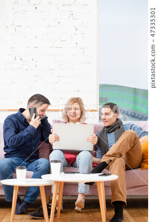 Friends sit on the couch, chatting and using a smartphone, desktop computer, laptop. Friends sit on the couch, chatting and using a smartphone, desktop computer, laptop. 47335301