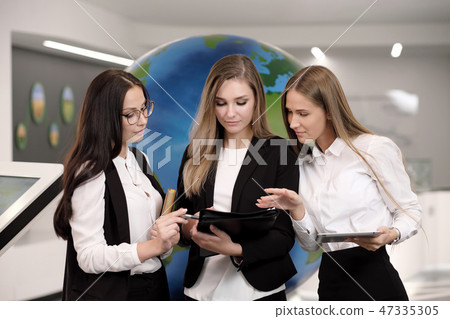 Three beautiful young girls in the office with a tablet on the background of the globe. Business and 47335305