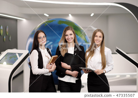 Three beautiful young girls in the office with a tablet on the background of the globe. Business and 47335507