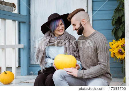 Young woman and man, family, sitting on porch of village house with pumpkins. 47335700