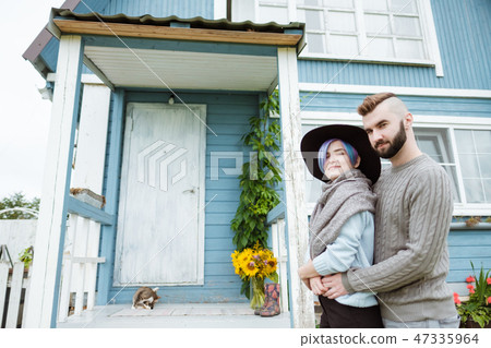 Young woman and man, family, sitting on porch of village house with pumpkins. 47335964
