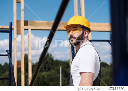 The man is a builder on the roof of a wooden frame house. 47337391