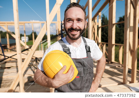 The man is a builder on the roof of a wooden frame house. 47337392