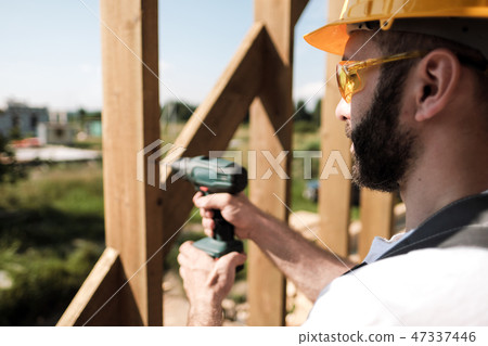 The man is a builder on the roof of a wooden frame house. 47337446