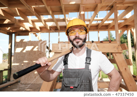 The man is a builder on the roof of a wooden frame house. 47337450