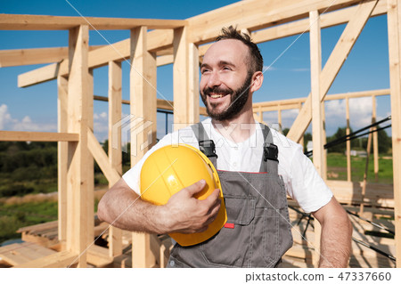 The man is a builder on the roof of a wooden frame house. 47337660