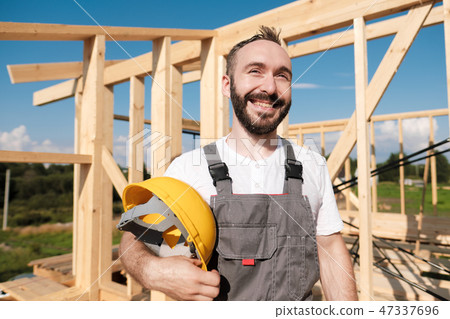 The man is a builder on the roof of a wooden frame house. 47337696