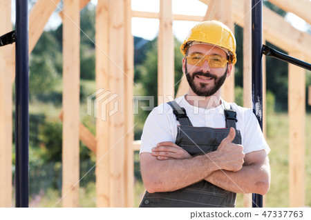The man is a builder on the roof of a wooden frame house. 47337763
