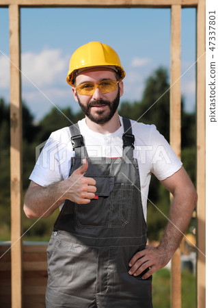 The man is a builder on the roof of a wooden frame house. 47337801