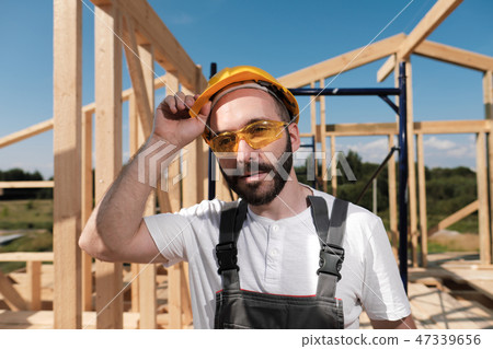 The man is a builder on the roof of a wooden frame house. 47339656