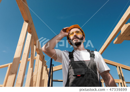The man is a builder on the roof of a wooden frame house. The man is a builder on the roof of a wooden frame house. 47339899