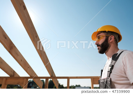 The man is a builder on the roof of a wooden frame house. The man is a builder on the roof of a wooden frame house. 47339900