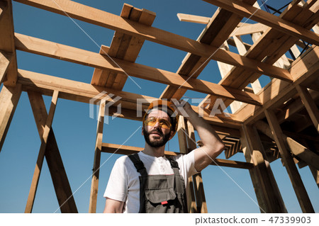 The man is a builder on the roof of a wooden frame house. The man is a builder on the roof of a wooden frame house. 47339903