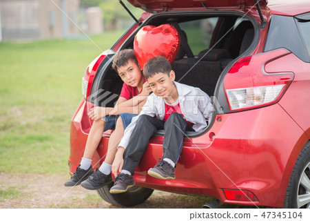 Little boys sitting on the back door of the car with balloon heart in hand Little boys sitting on the back door of the car with balloon heart in hand 47345104