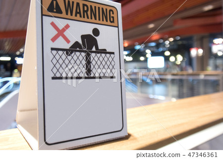 Close-up image a white warning don't climb over the fence signage is displayed on glass barrier in departments store. 47346361