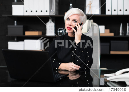 Beautiful woman talking on phone sitting at table in office Beautiful woman talking on phone sitting at table in office 47349038