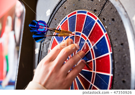Person's hand removing arrows from dartboard 47350926
