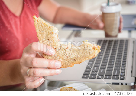 Eating a breakfast sandwich while working Eating a breakfast sandwich while working 47353182