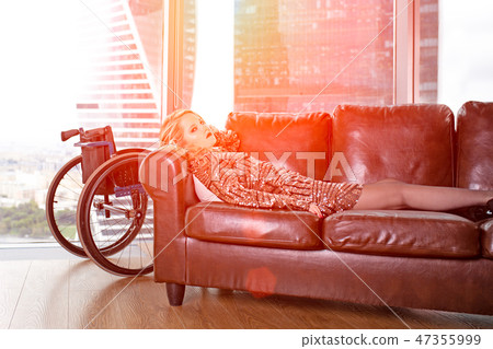 A beautiful young blonde girl in a fashionable dress with a disability, posing on a leather sofa A beautiful young blonde girl in a fashionable dress with a disability, posing on a leather sofa 47355999