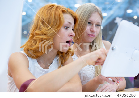 two young beautiful women in a travel agency choosing a vacation trip, using the interactive screen. two young beautiful women in a travel agency choosing a vacation trip, using the interactive screen. 47356296